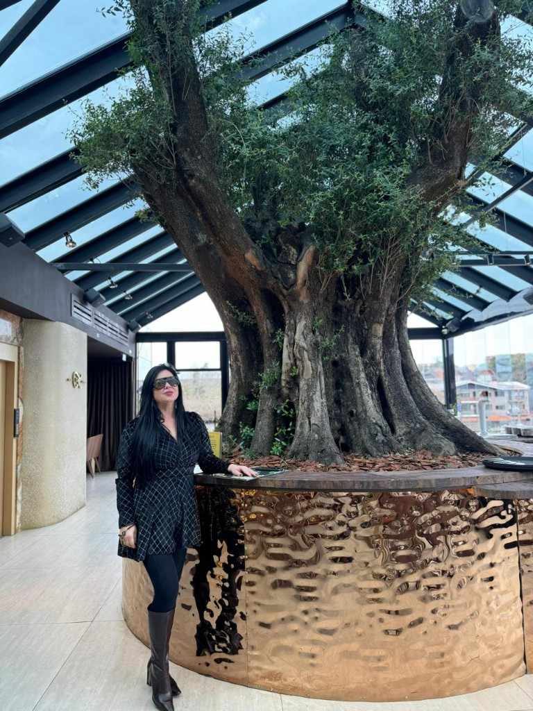 Ângela Marcon ao lado de oliveira centenária com mais de 500 anos instalada no Casa Lugano em Gramado RS
